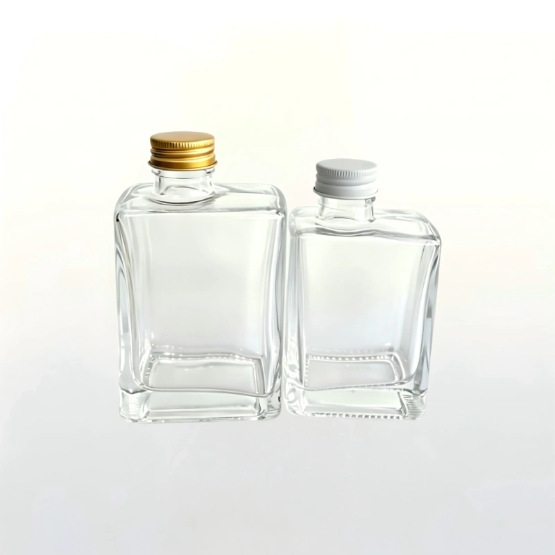 Two clear glass liquor bottles with gold and silver aluminum screw caps against a white background.
